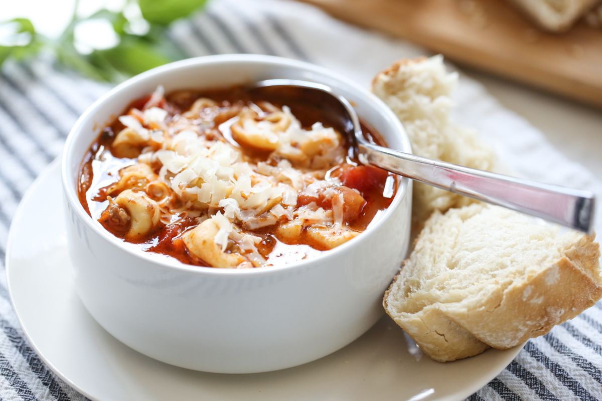 tortellini soup in a white bowl with a spoon and side of bread