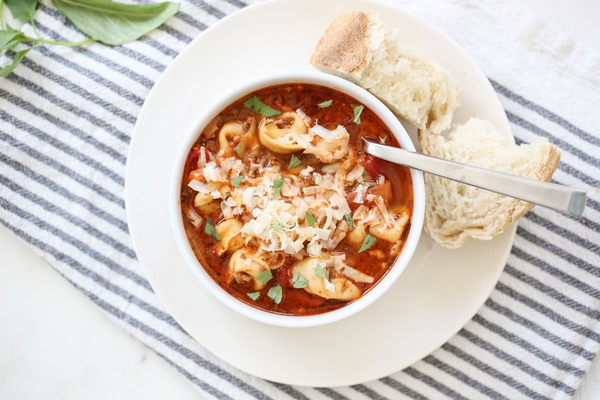 Tortellini sausage soup in a white bowl with a side of bread