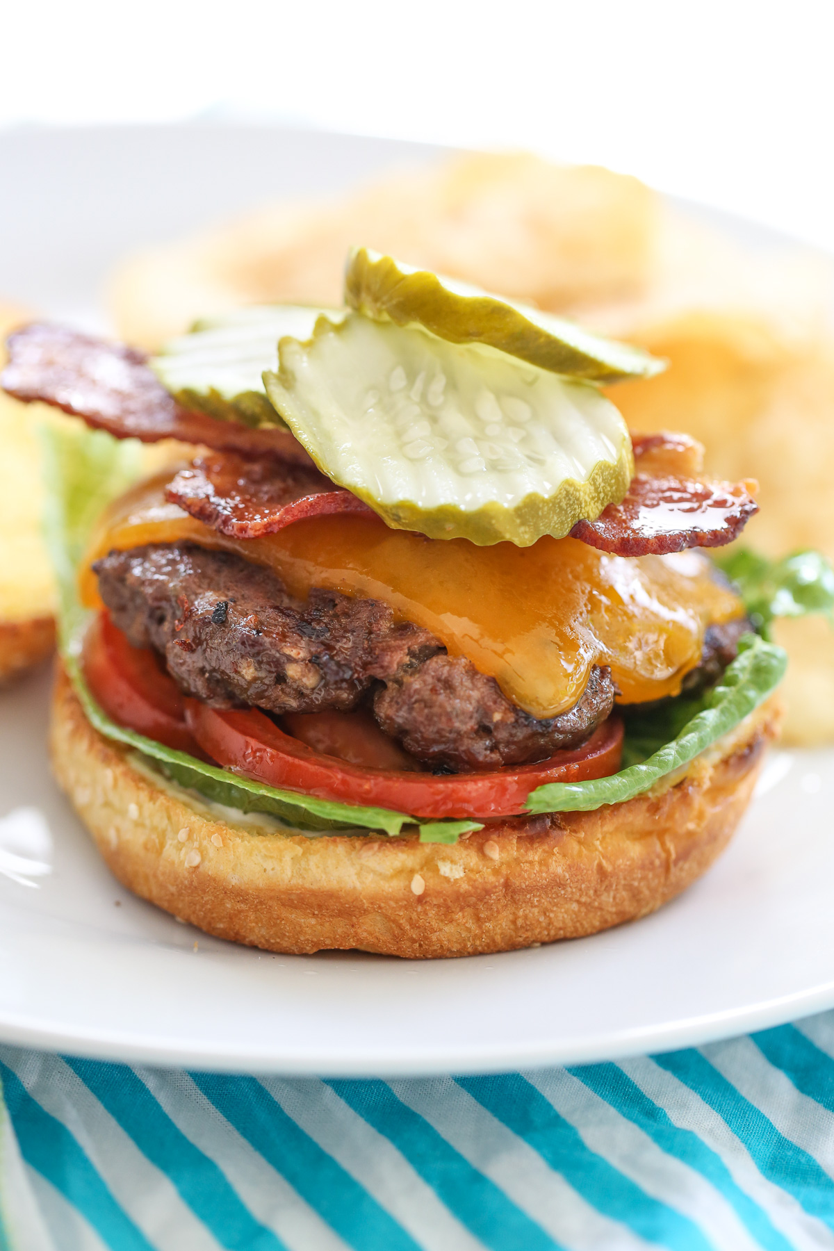 Cheeseburger with toppings on a while plate with chips in the background