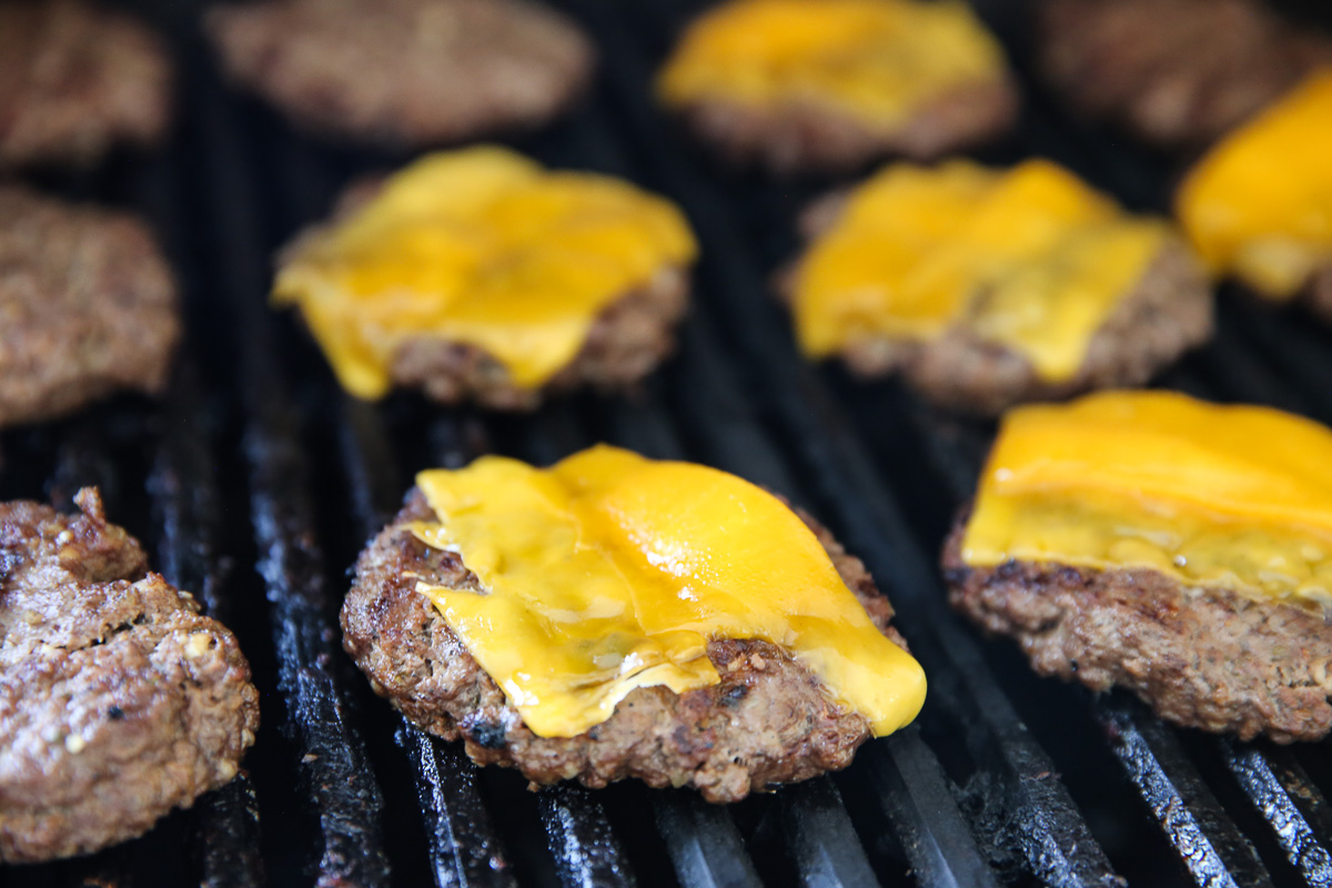 hamburgers cooking on a grill with melted cheese on top