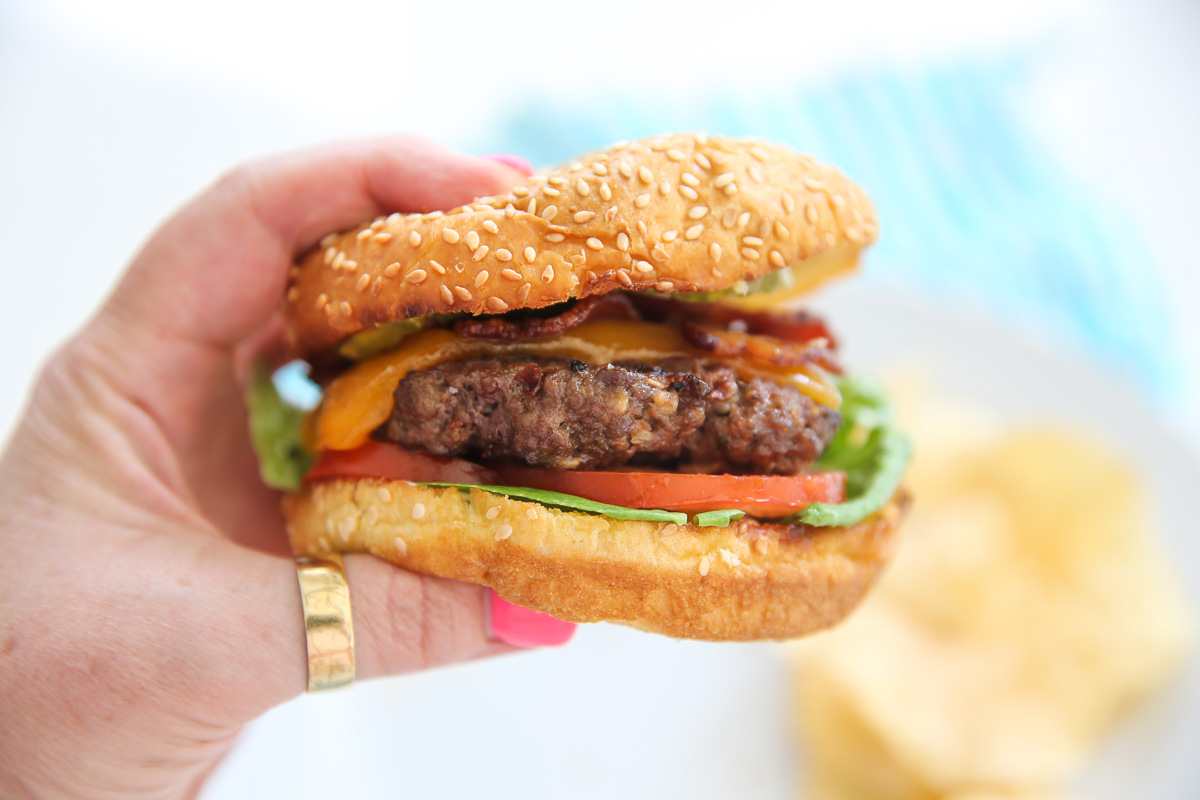 Hand holding a hamburger with lots of toppings on it
