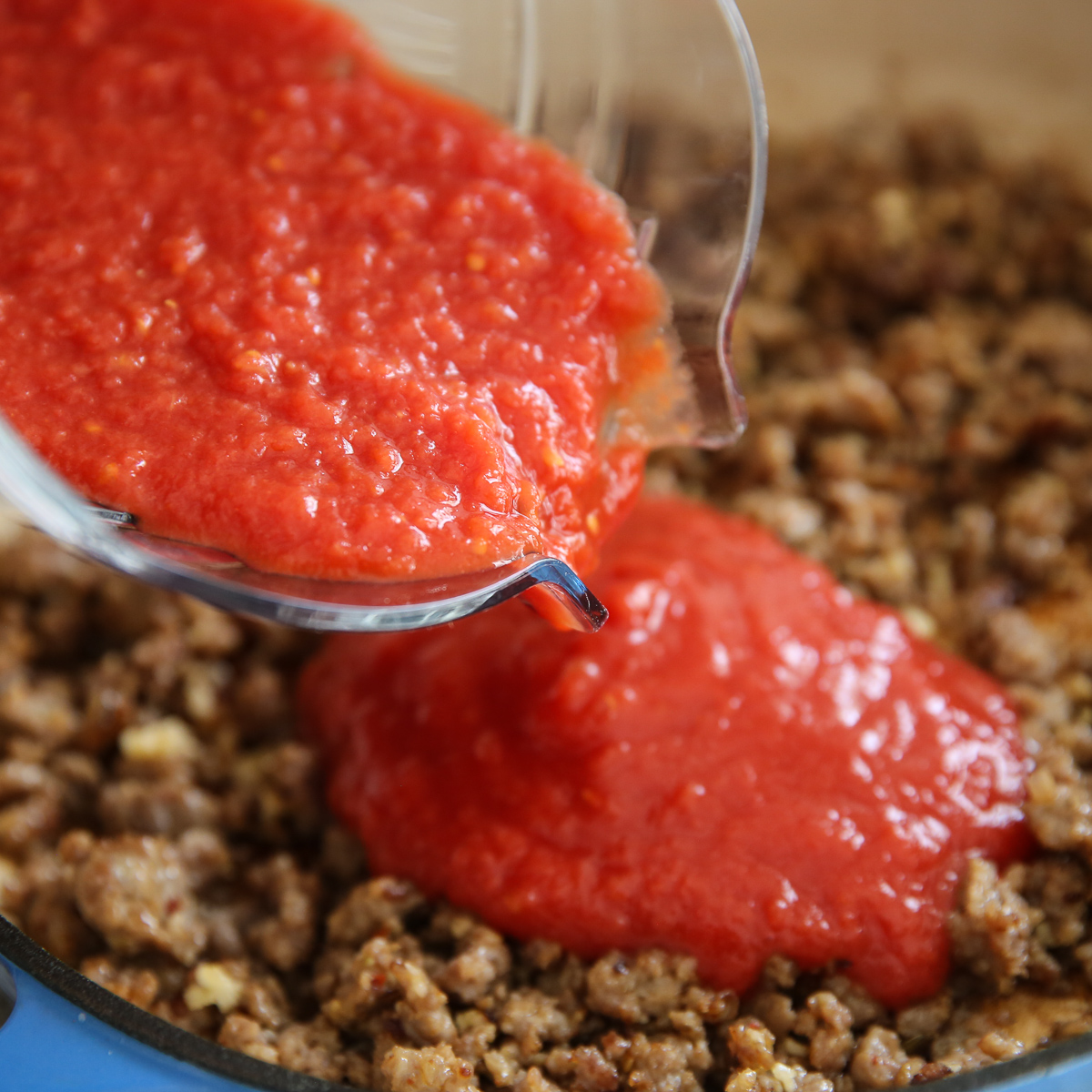 pouring tomato sauce into cooked sausage