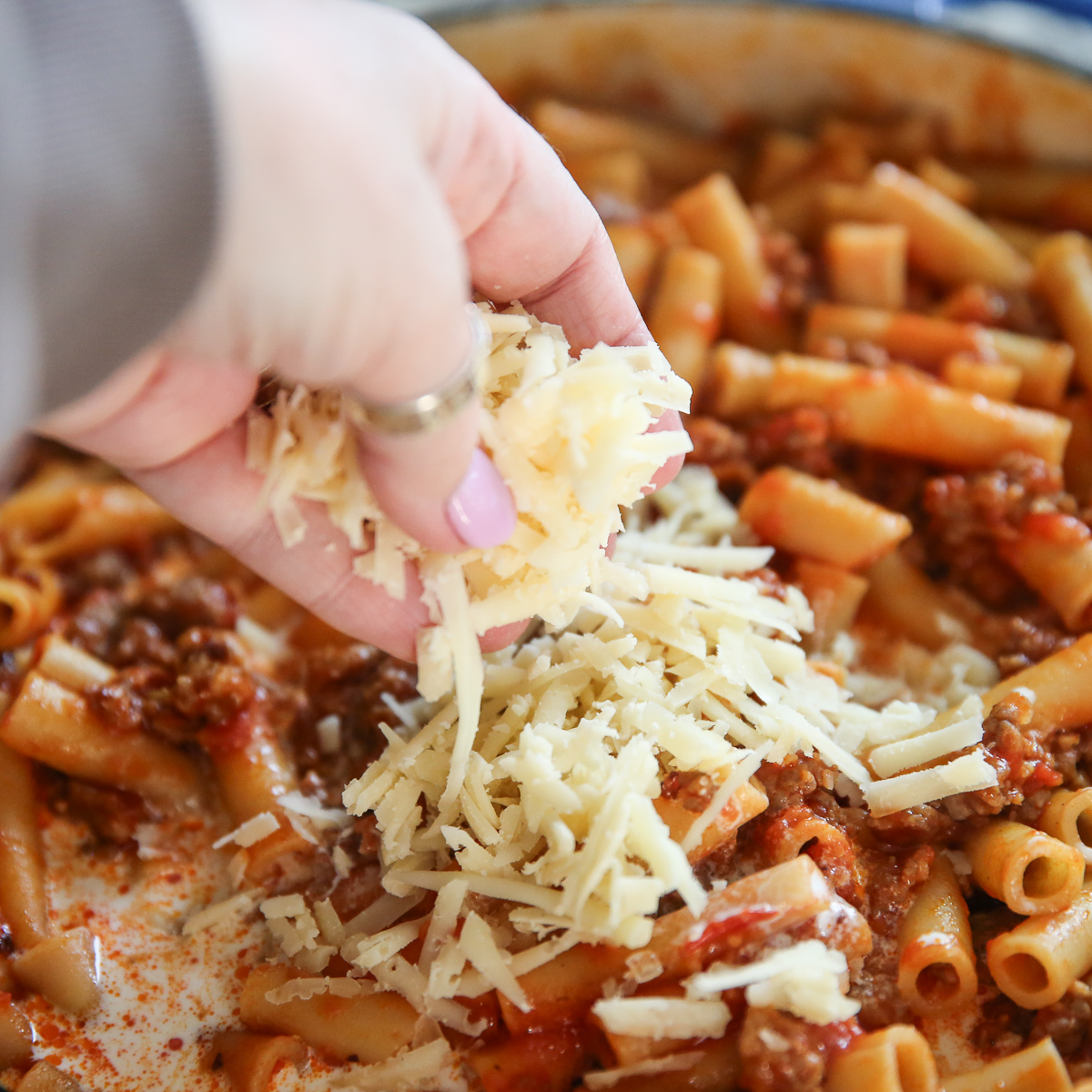 Sprinkling cheese on a pan of Skillet Baked Ziti from Our Best Bites