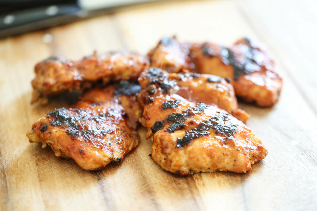 Barbecued chicken thighs on a cutting board.