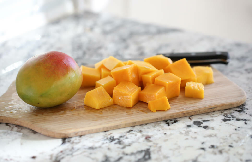 A mango and mango chunks on a cutting board.