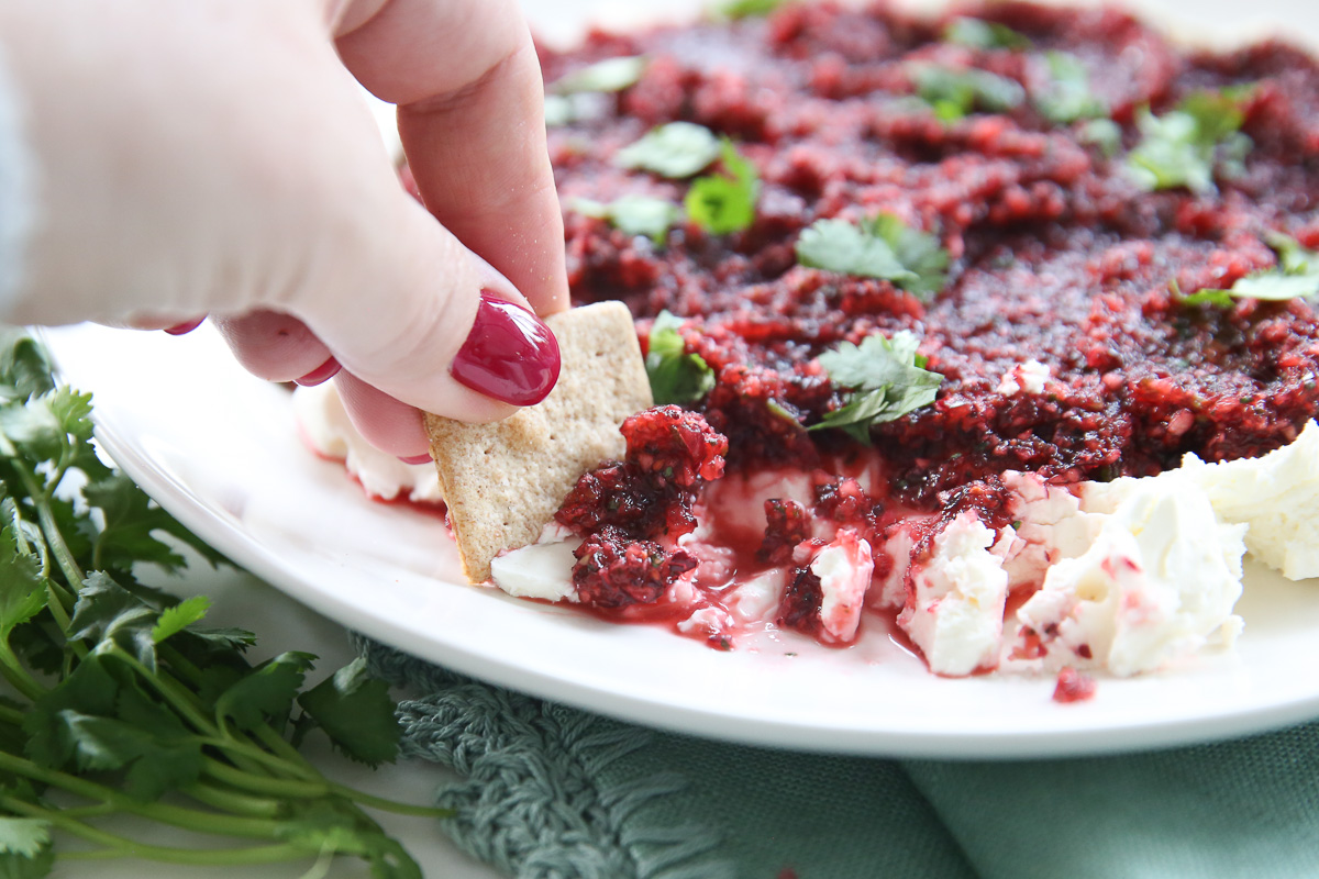 hand scooping cranberry salsa onto cracker