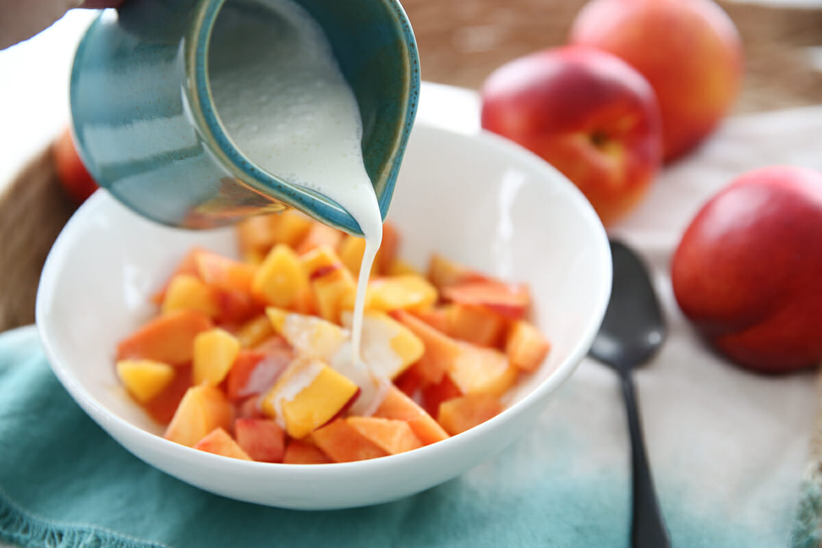cream being poured over fresh peaches