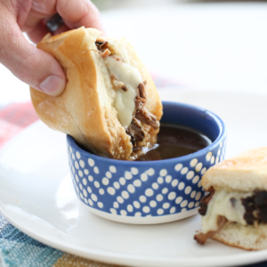 A sandwich with beef and cheese being dipped in au jus.