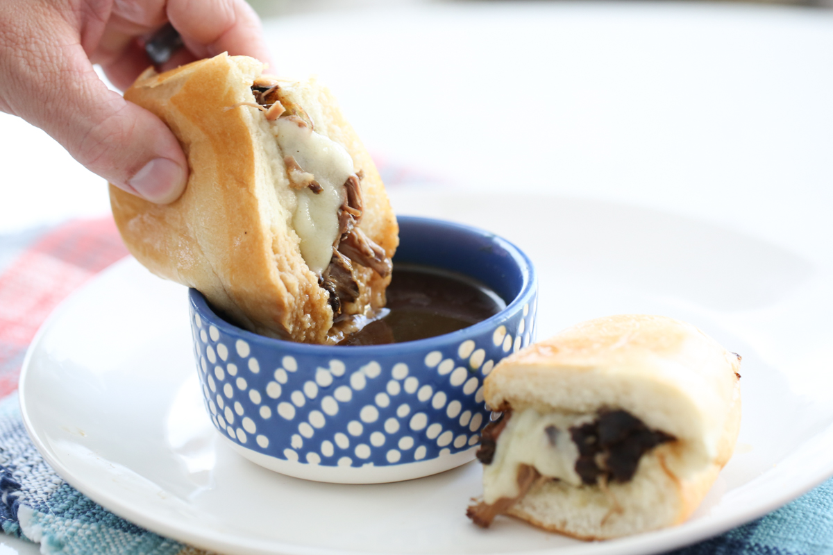 A sandwich with beef and cheese being dipped in au jus.