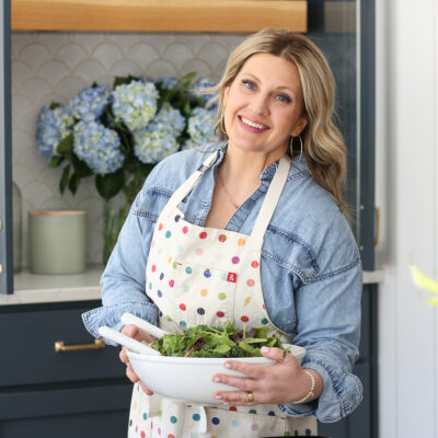 Woman in apron holding salad bar in front of blue flowers