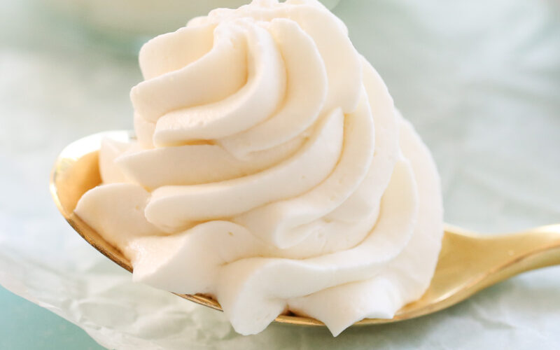 Whipped cream frosting piped onto a spoon that is resting on parchment paper.