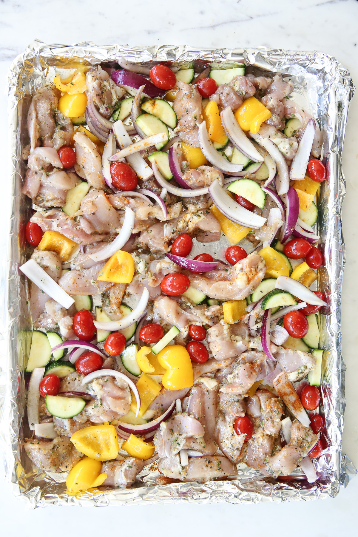 raw chicken and vegetables on a sheet pan