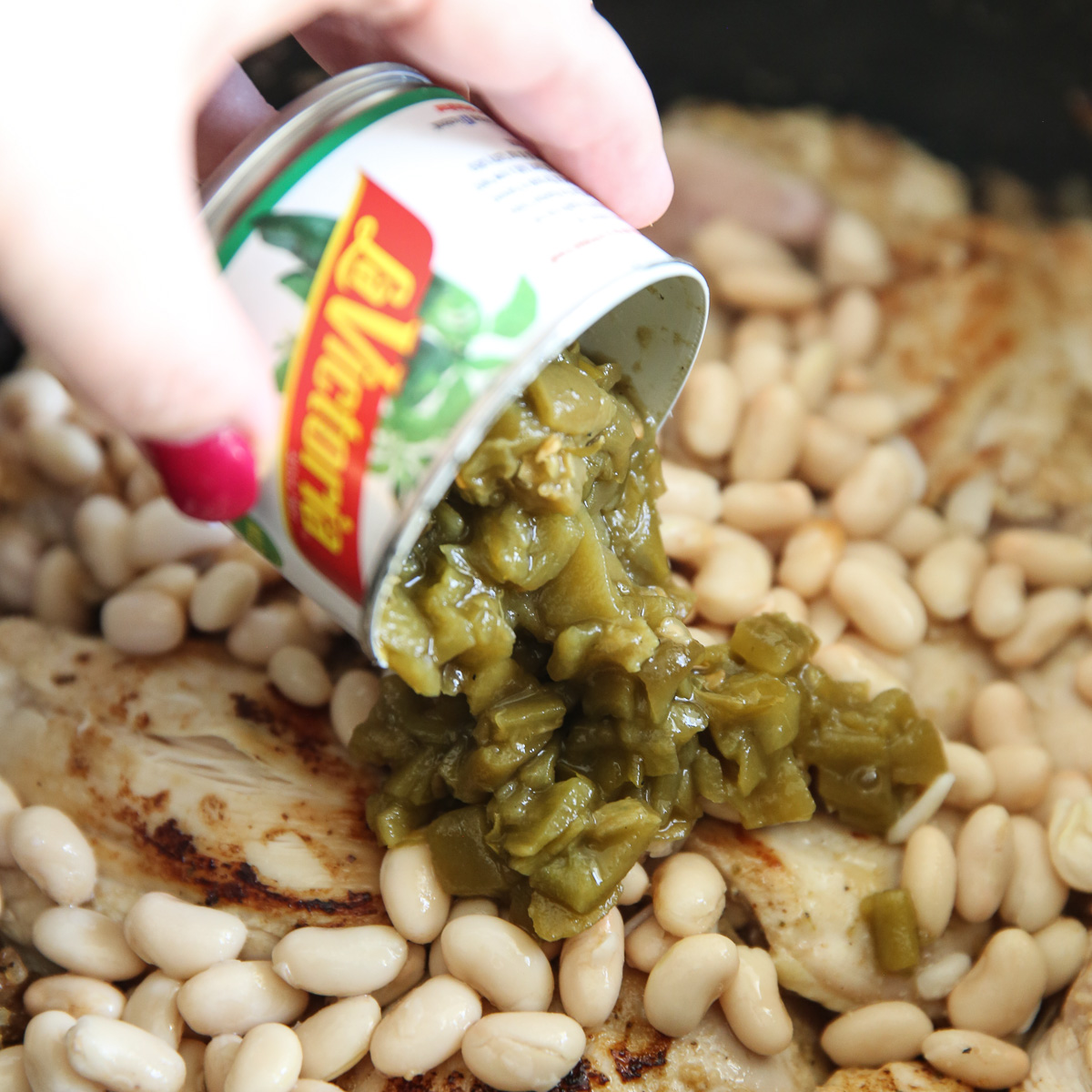 adding green chilis to pot of chicken stew