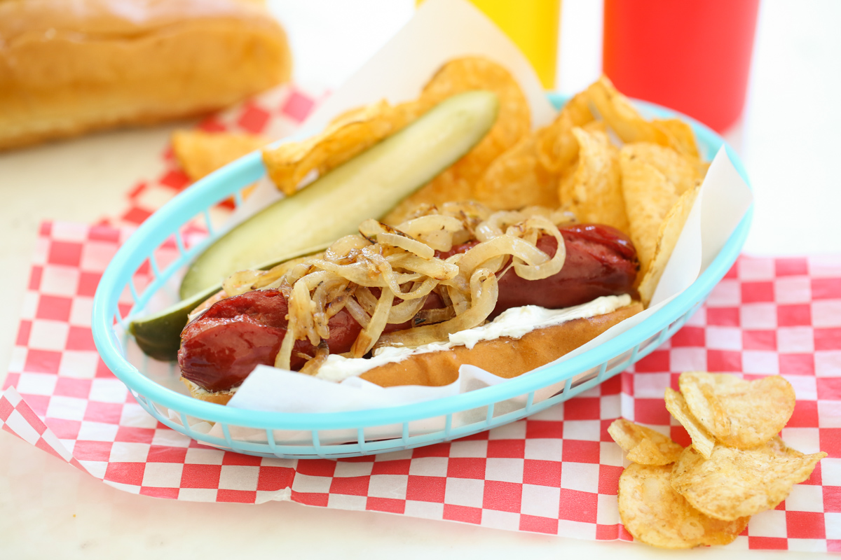 Seattle Style hot dog in a basket with chips and a pickle