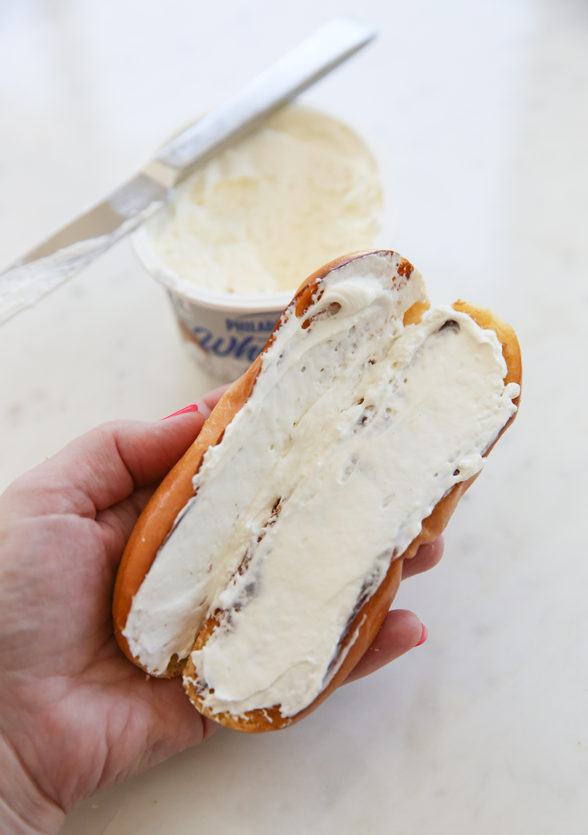 spreading cream cheese on a hot dog bun