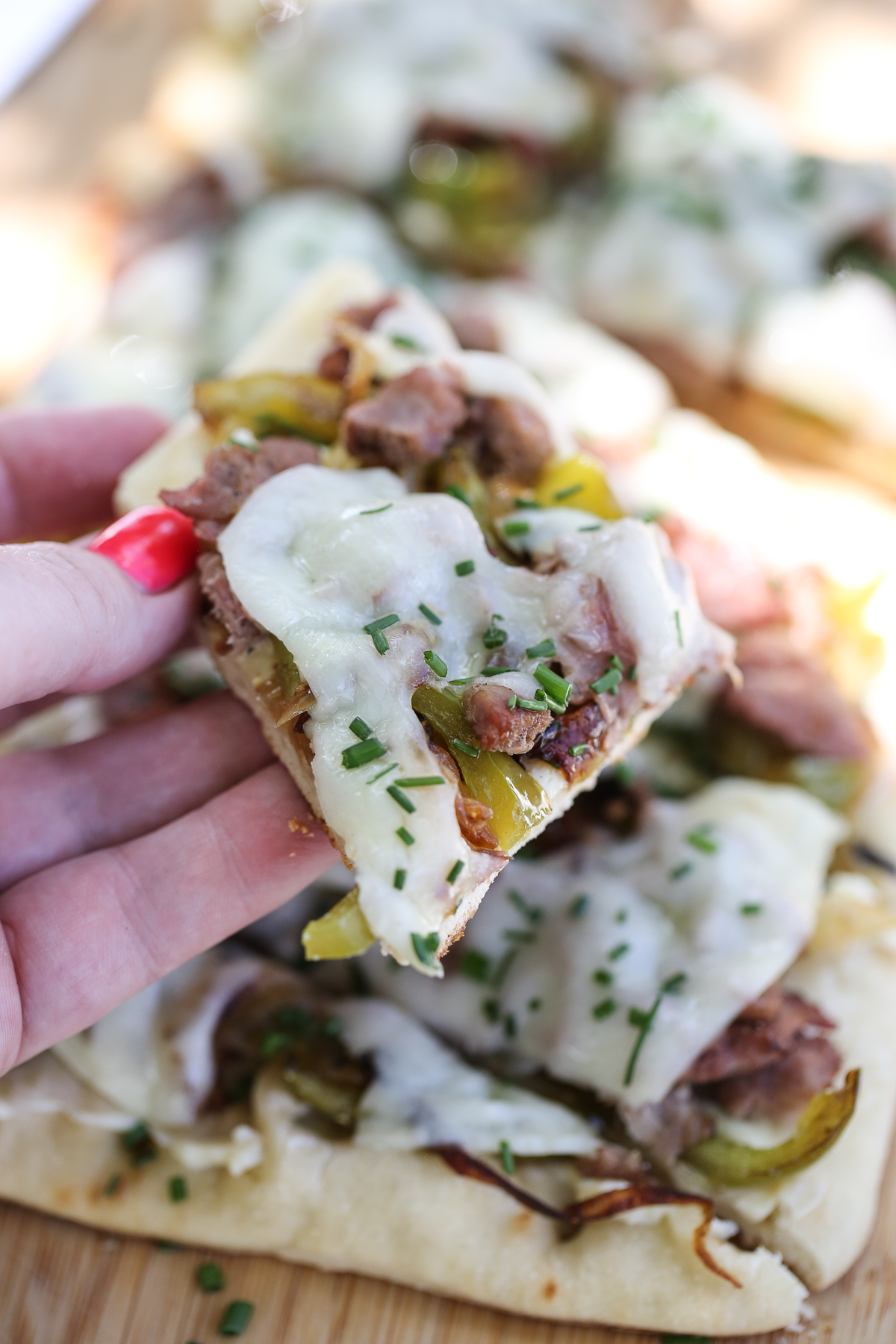 hand holding a bite of cheesesteak flatbread