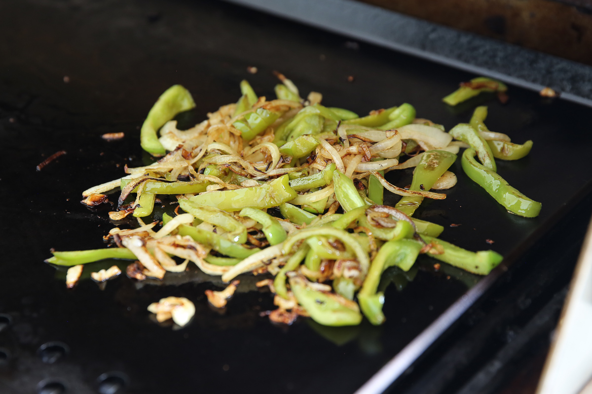 peppers and onions cooking on a flat top
