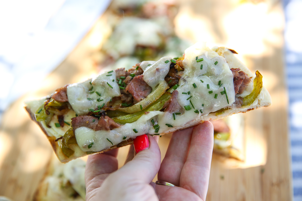 hand holding a slice of Cheesesteak flatbread
