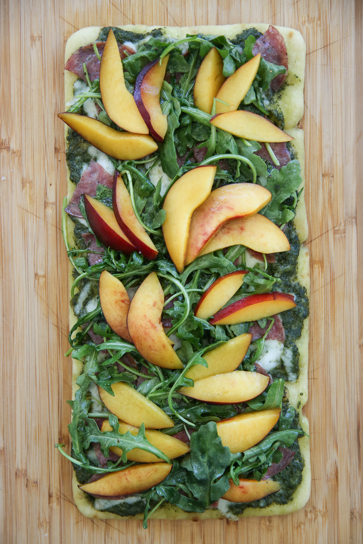 Cooked flatbread with salami and cheese and greens and nectarines