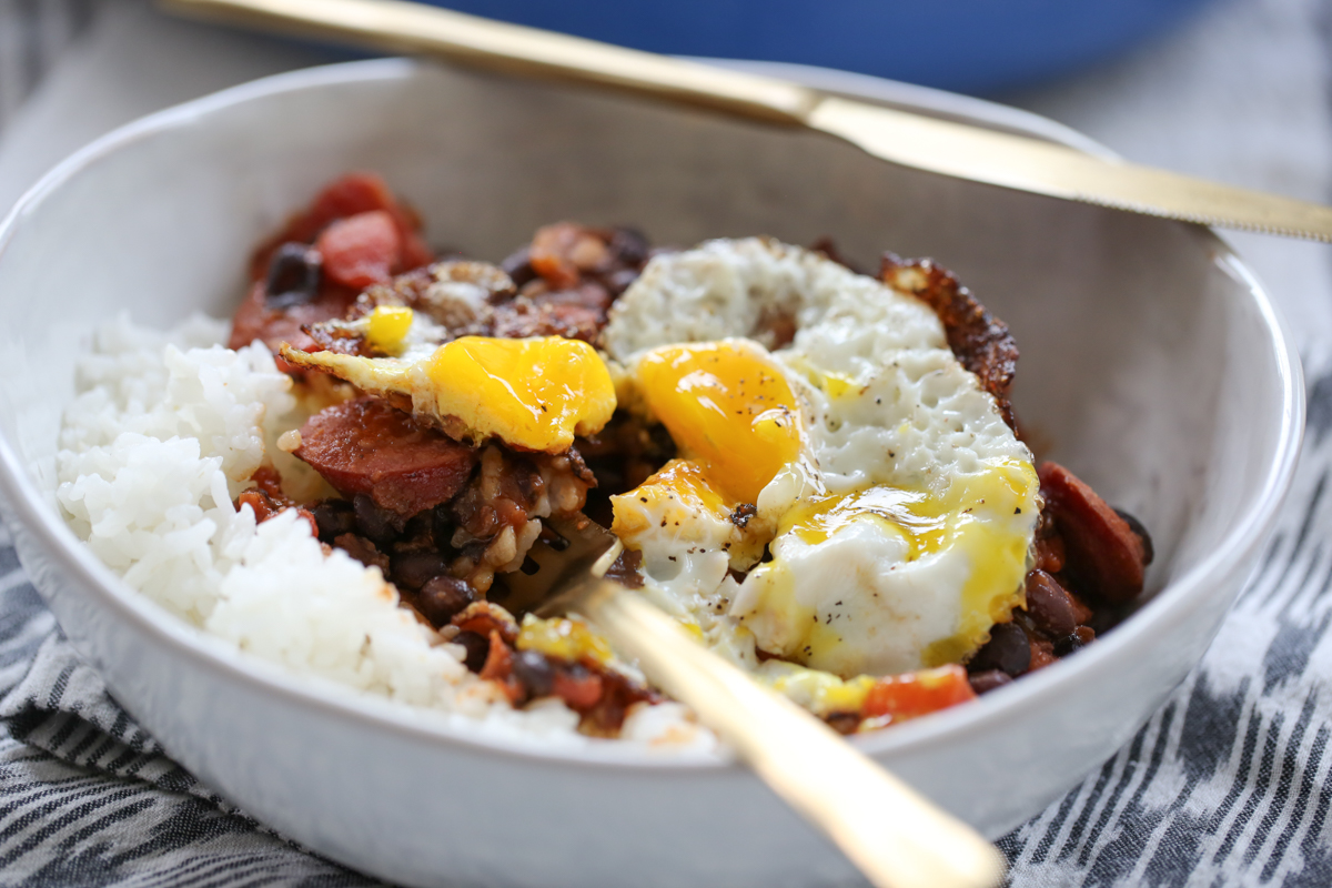 black bean and kielbasa skillet in a bowl over rice with a broken fried egg on top