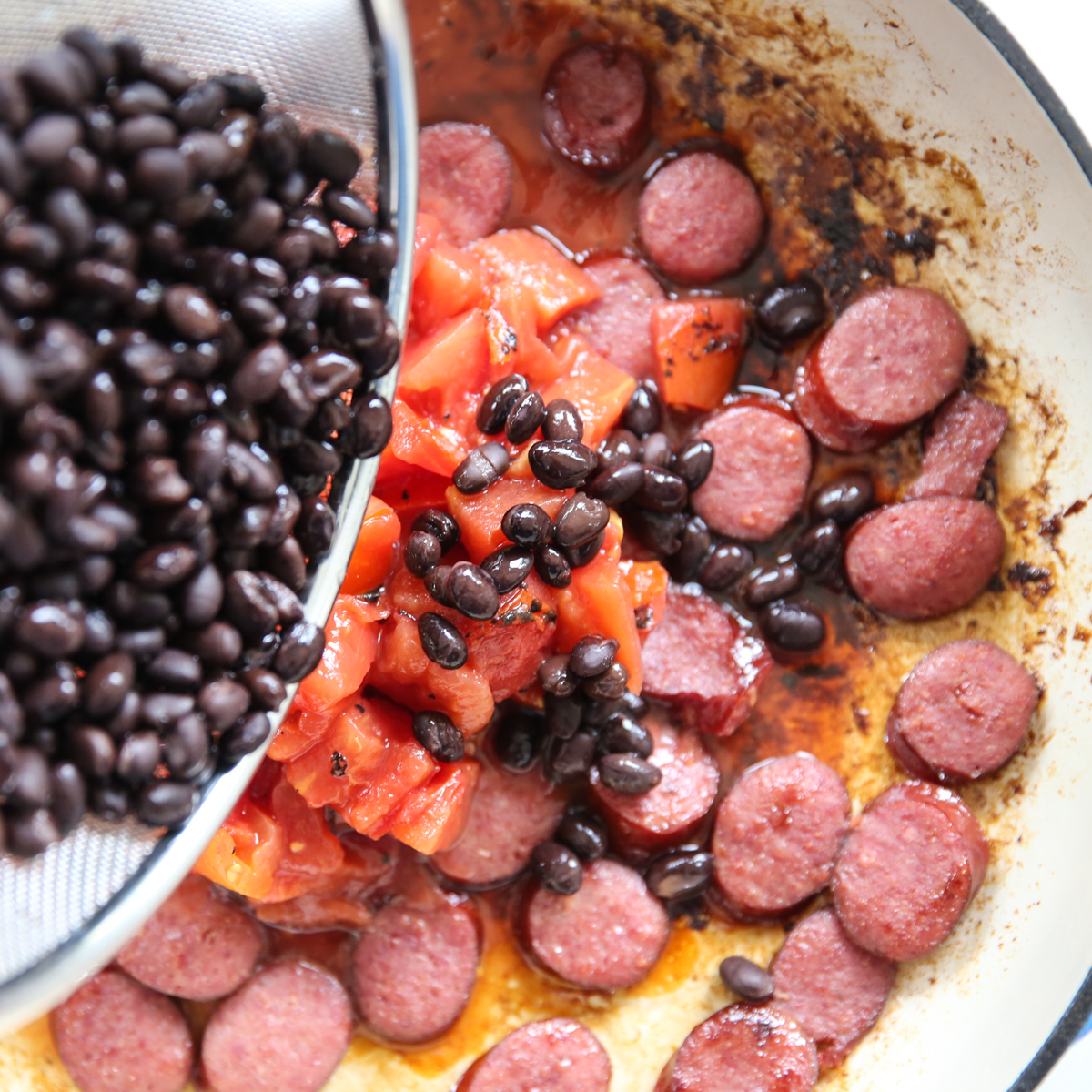 pouring black beans into a skillet