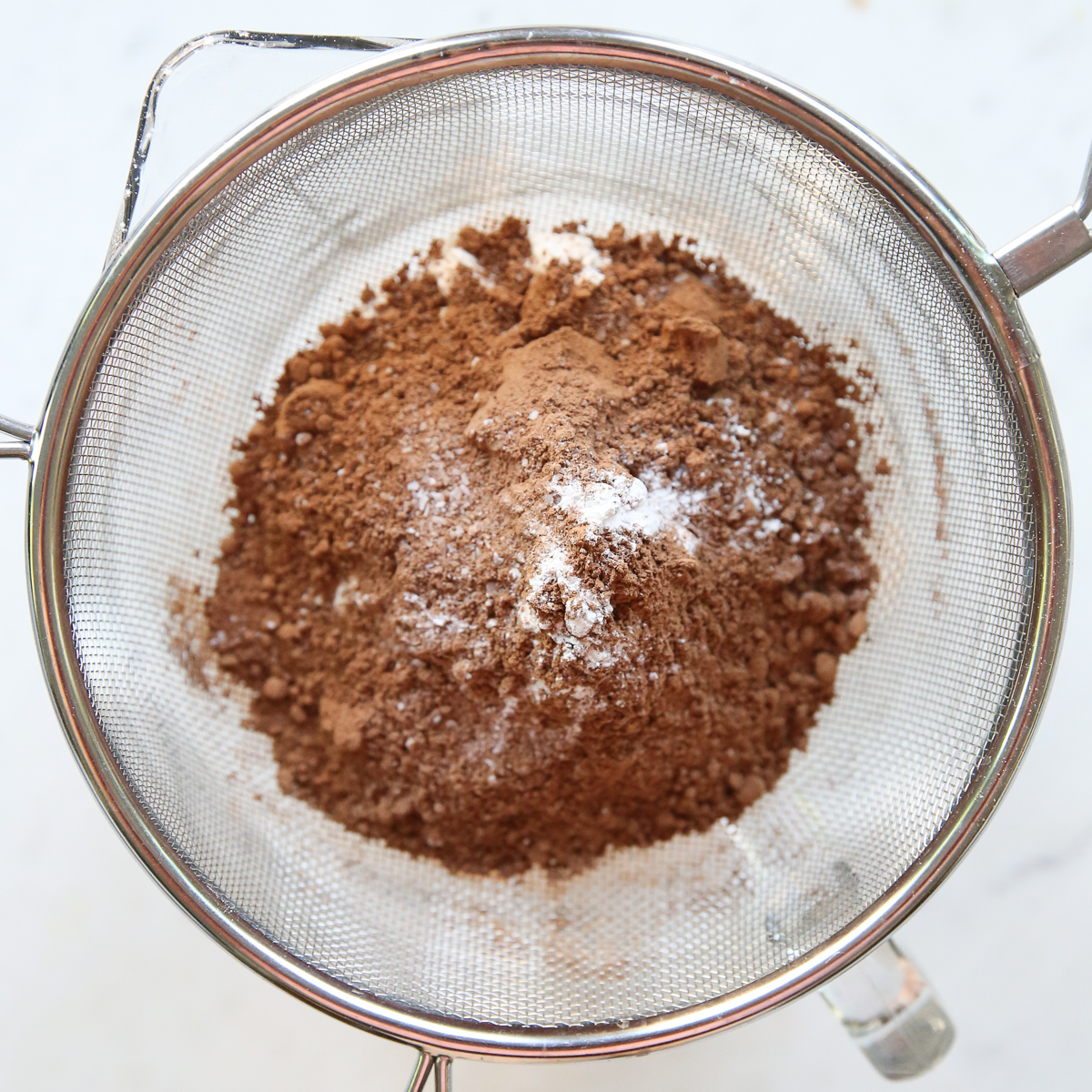 sifting chocolate in a glass bowl