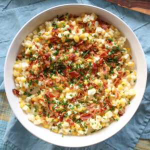creamed corn in a white bowl with bacon and chives over the top