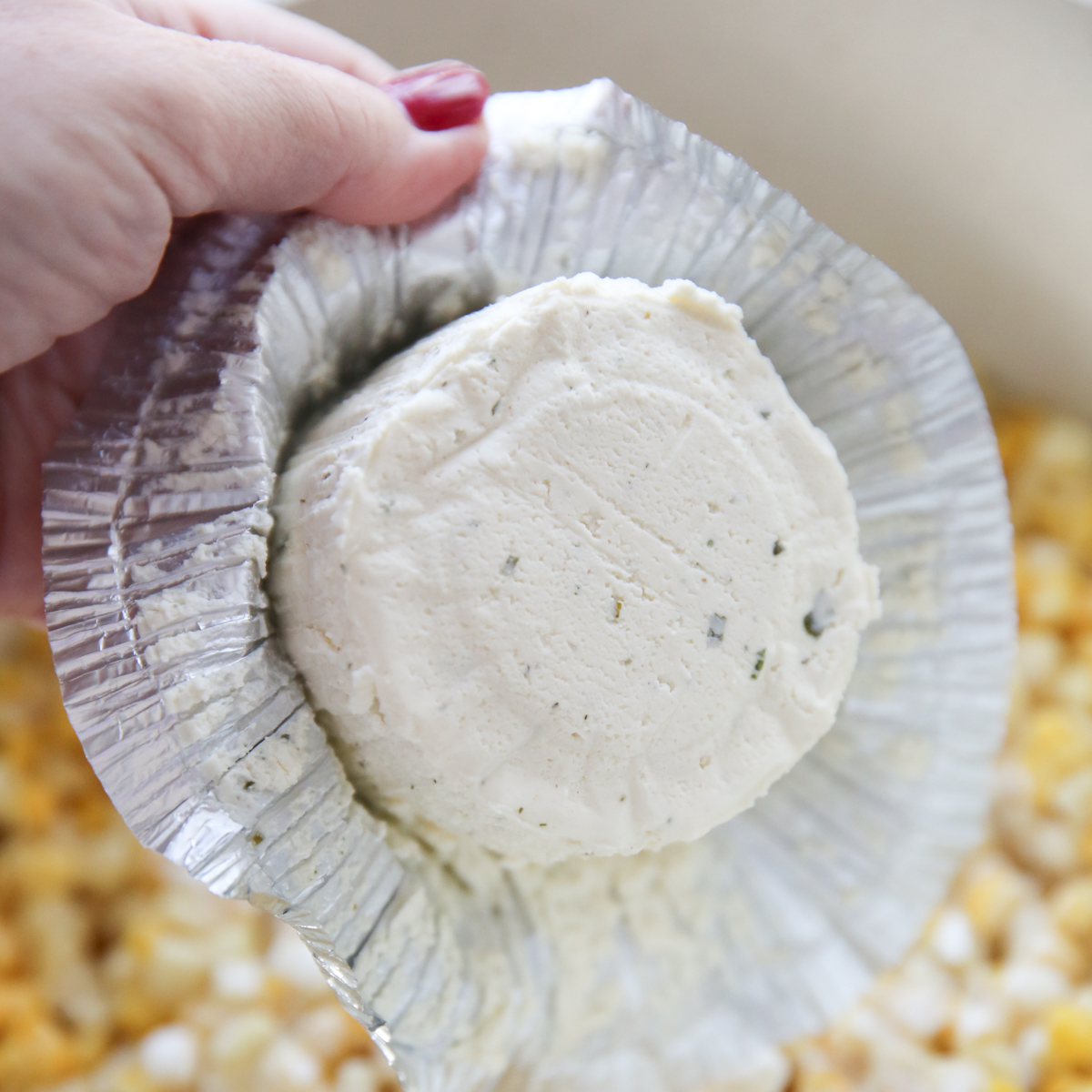 boursin cheese held over a pot of corn