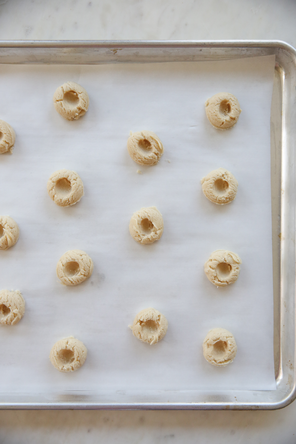 balls of cookie dough on a baking sheet with finger indentations
