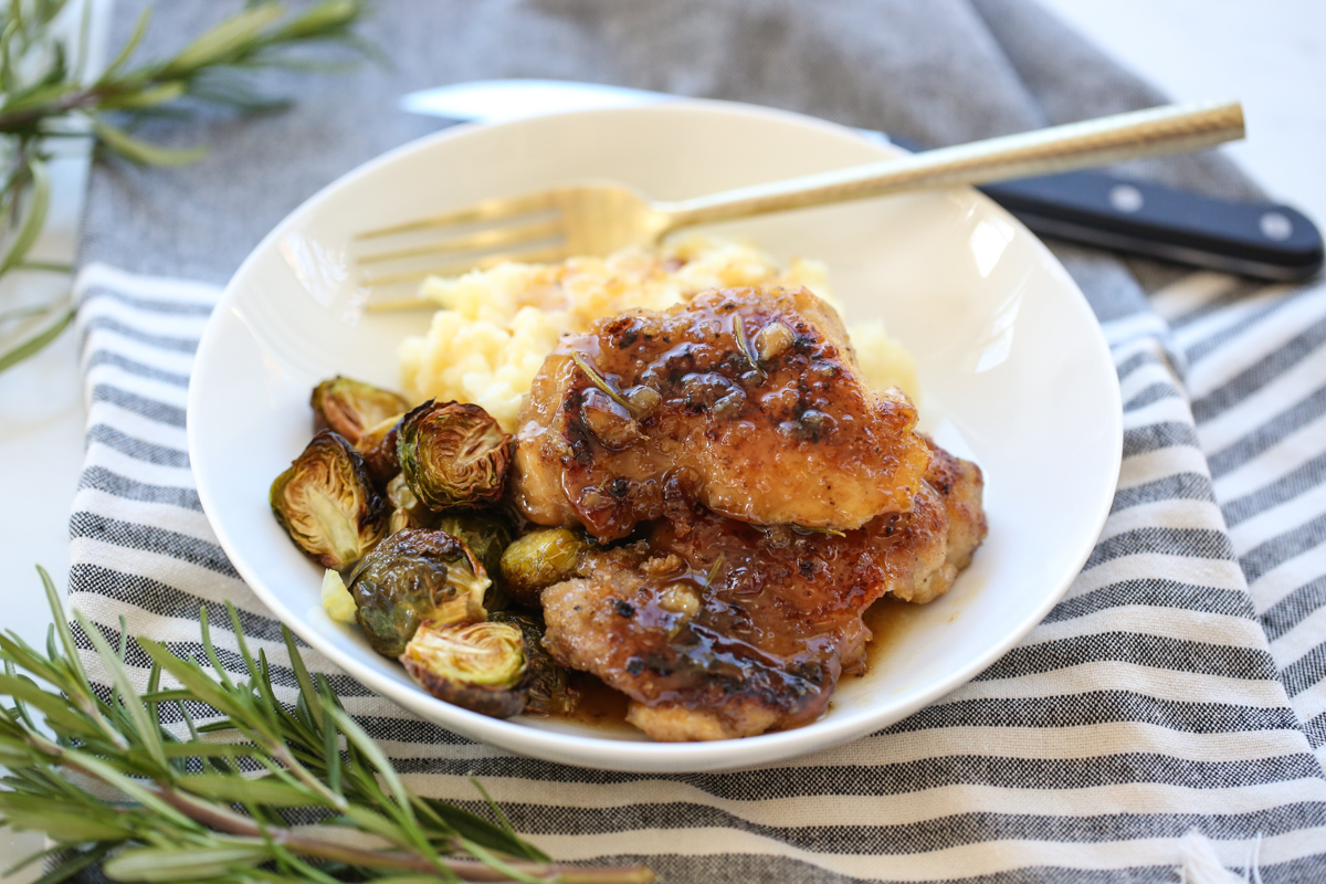 glazed chicken thighs on a serving plate with potatoes and brussells sprouts