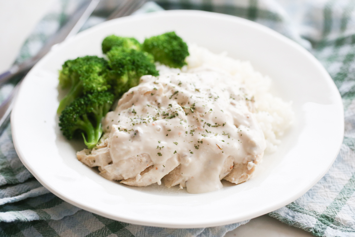 creamy sauce over chicken and rice on a plate with broccoli