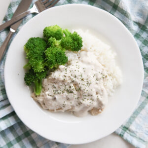 creamy sauce over chicken and rice on a plate with broccoli