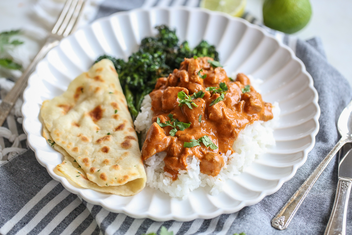 Butter chicken over rice with flatbread and broccoli, on a white plate