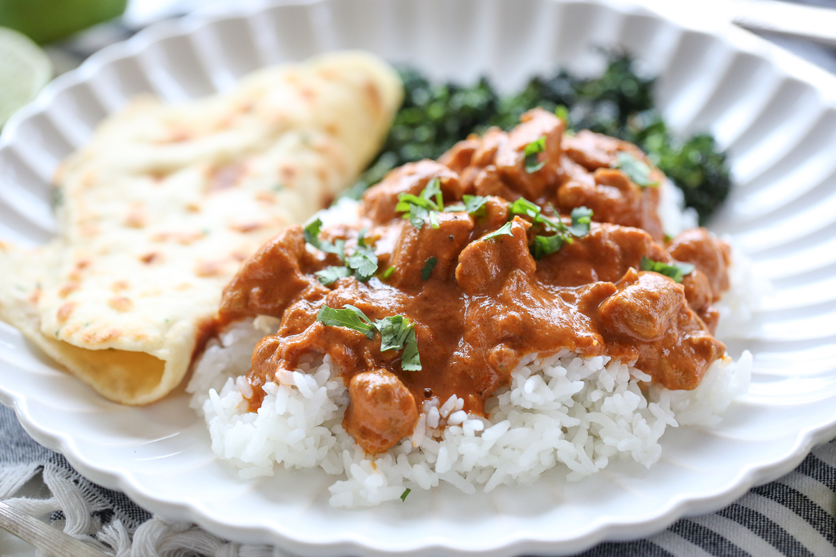 Butter chicken over rice with flatbread and broccoli, on a white plate