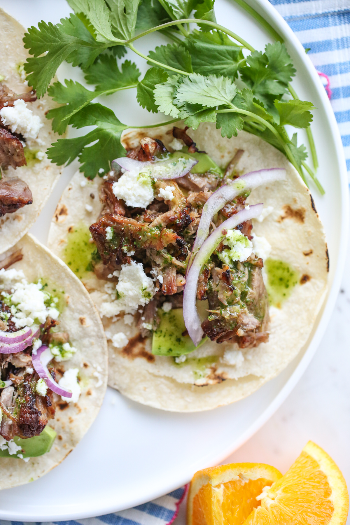 a white plate full of carnitas with cheese, onions, and cilantro