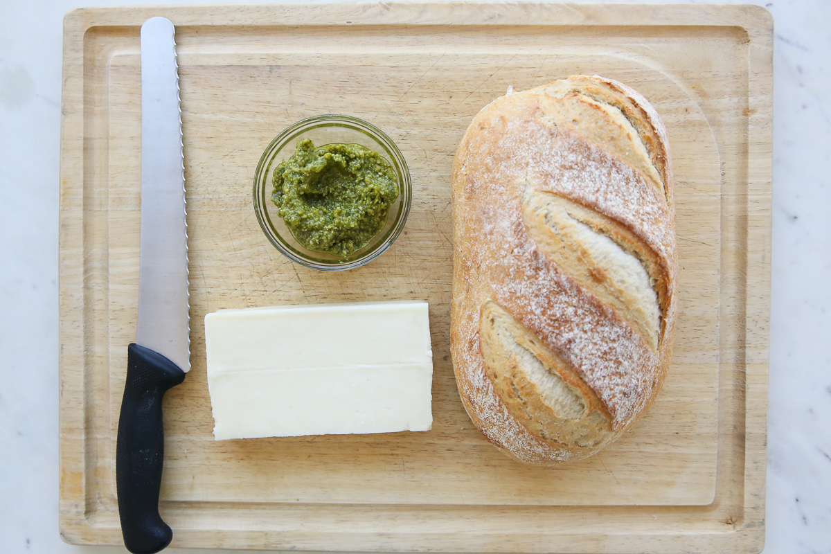 loaf of bread with cheese and pesto on a cutting board