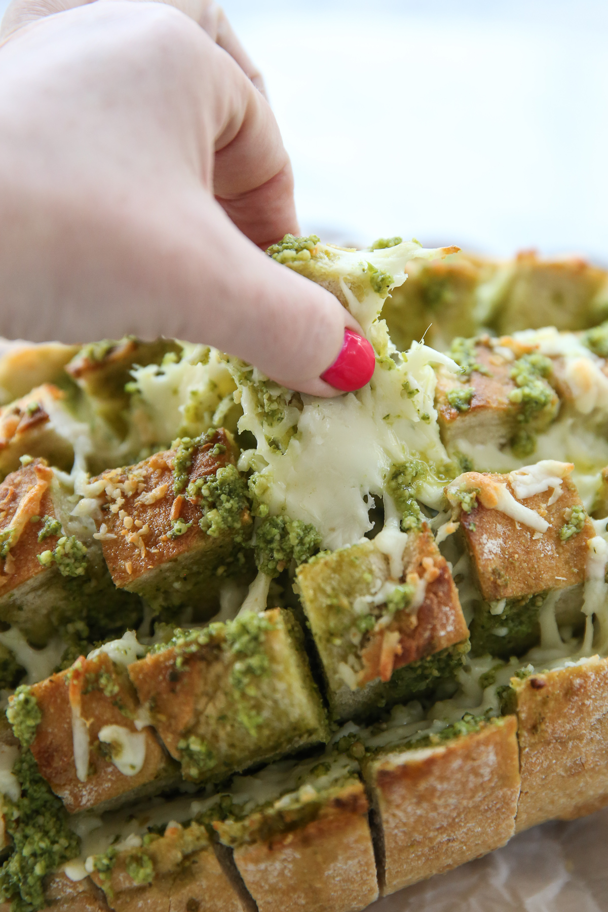 hand pulling up a piece of garlic pesto bread with cheese