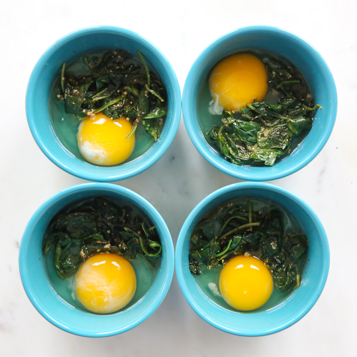raw eggs in ramekins with wilted spinach