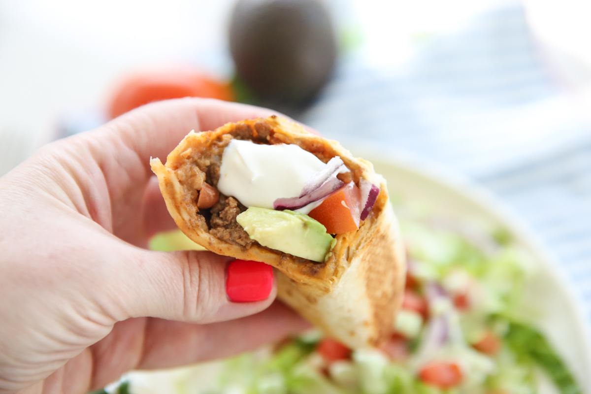 hand holding a burrito stuffed with bean, beef, and cheese.