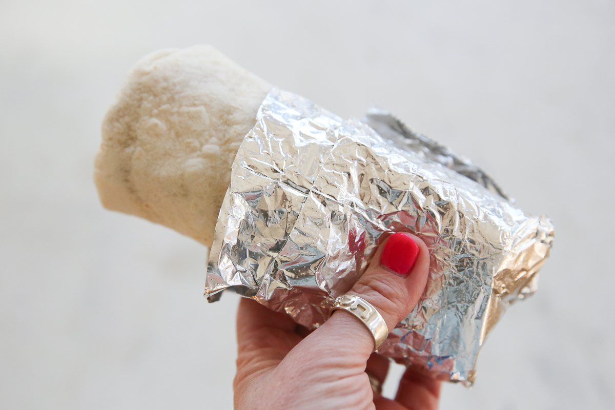 a person's hand holding a burrito wrapped in foil
