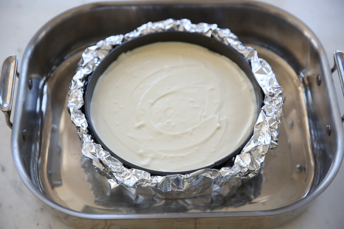 cheesecake pan wrapped in foil in a roasting pan