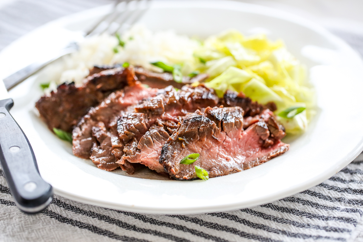 Sliced Ginger Soy Flank Steak on a plate with rice and cabbage