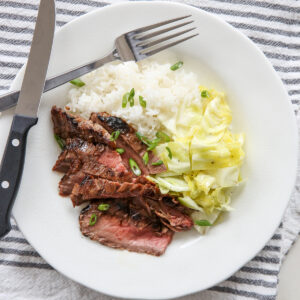 Sliced Ginger Soy Flank Steak on a plate with rice and cabbage