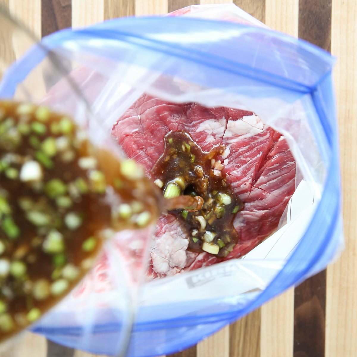 Pouring marinade into a Ginger Soy Flank Steak in a zip top bag
