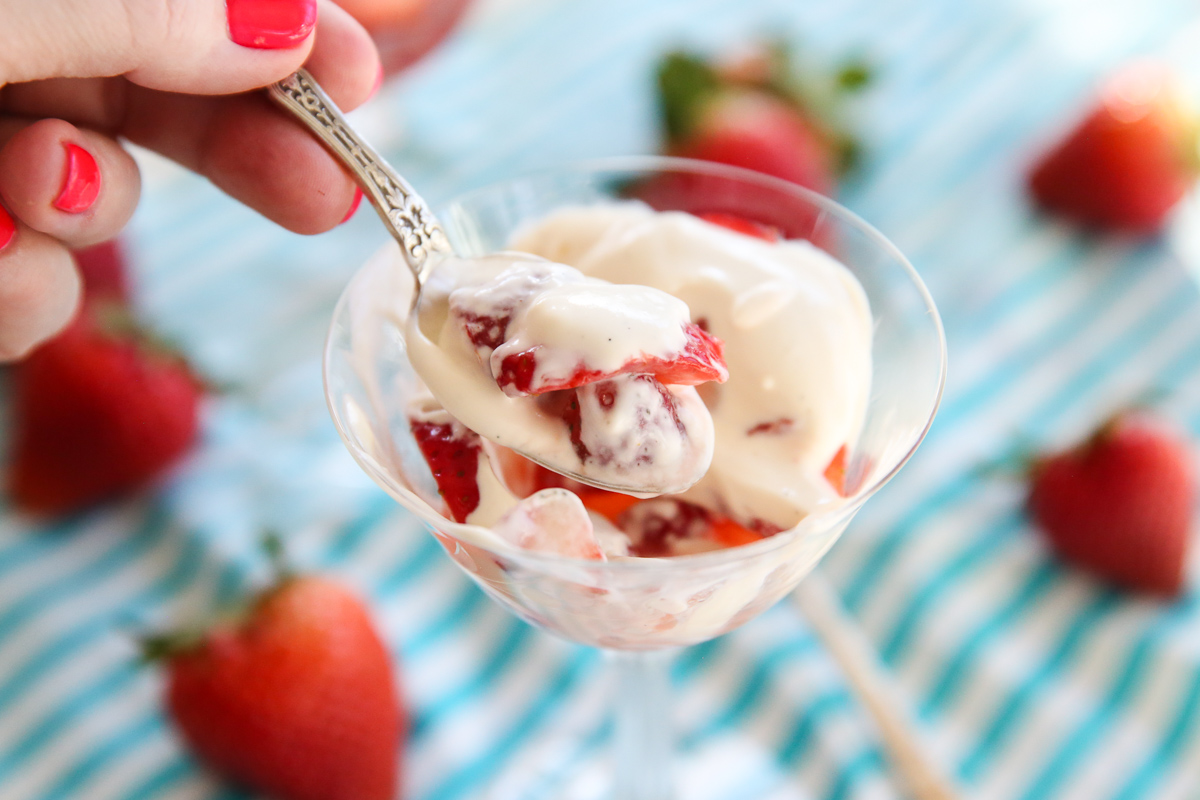 taking a spoonful of sliced berries in a goblet with cream on top