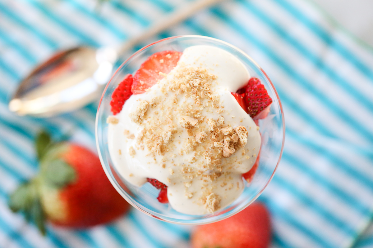 crumbled cookies on top of a crystal glass with sliced strawberries and cream