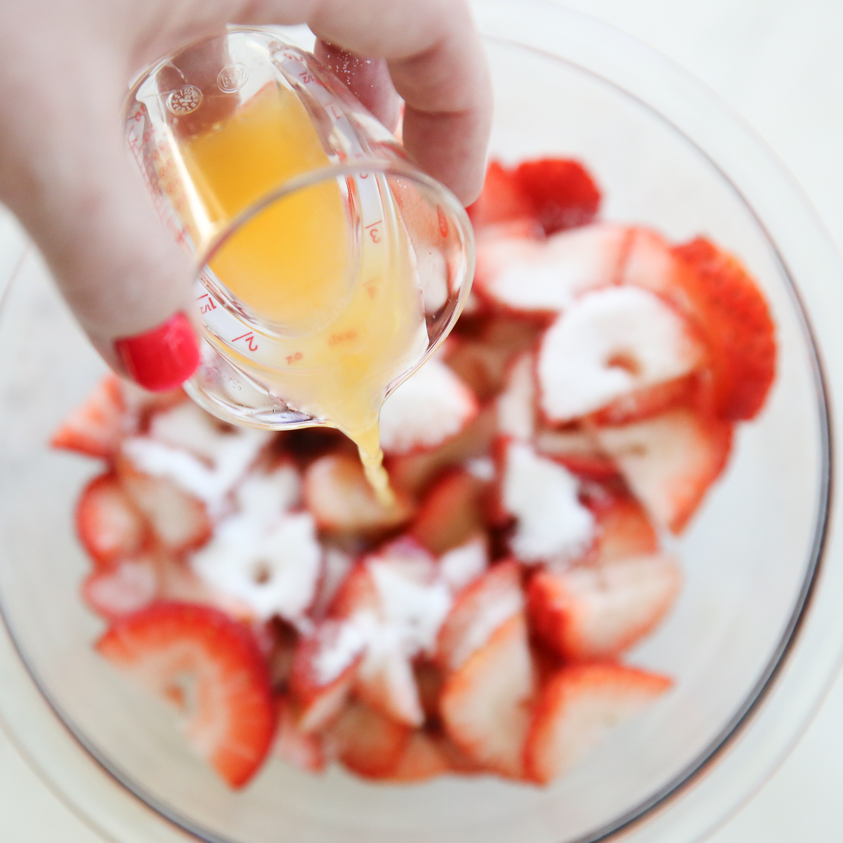 pouring orange juice into a bowl of strawberries with sugar on top