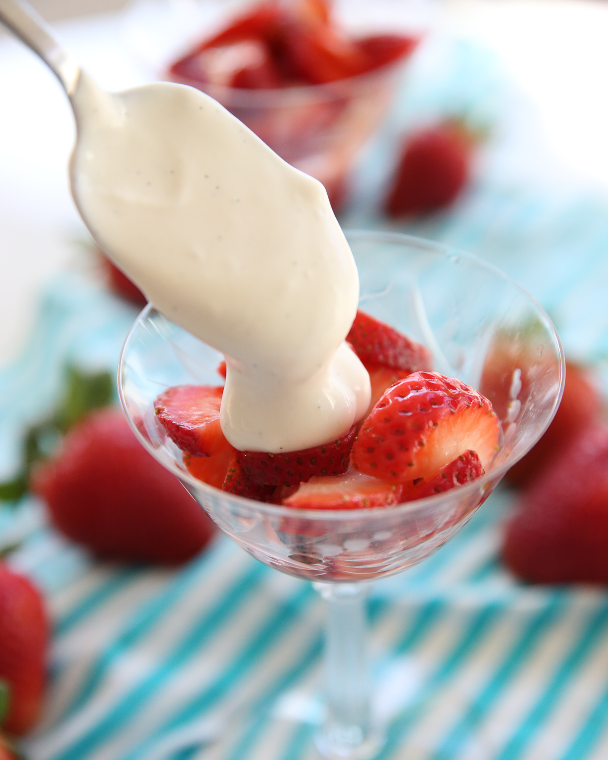 spooning cream on top of strawberries in a glass