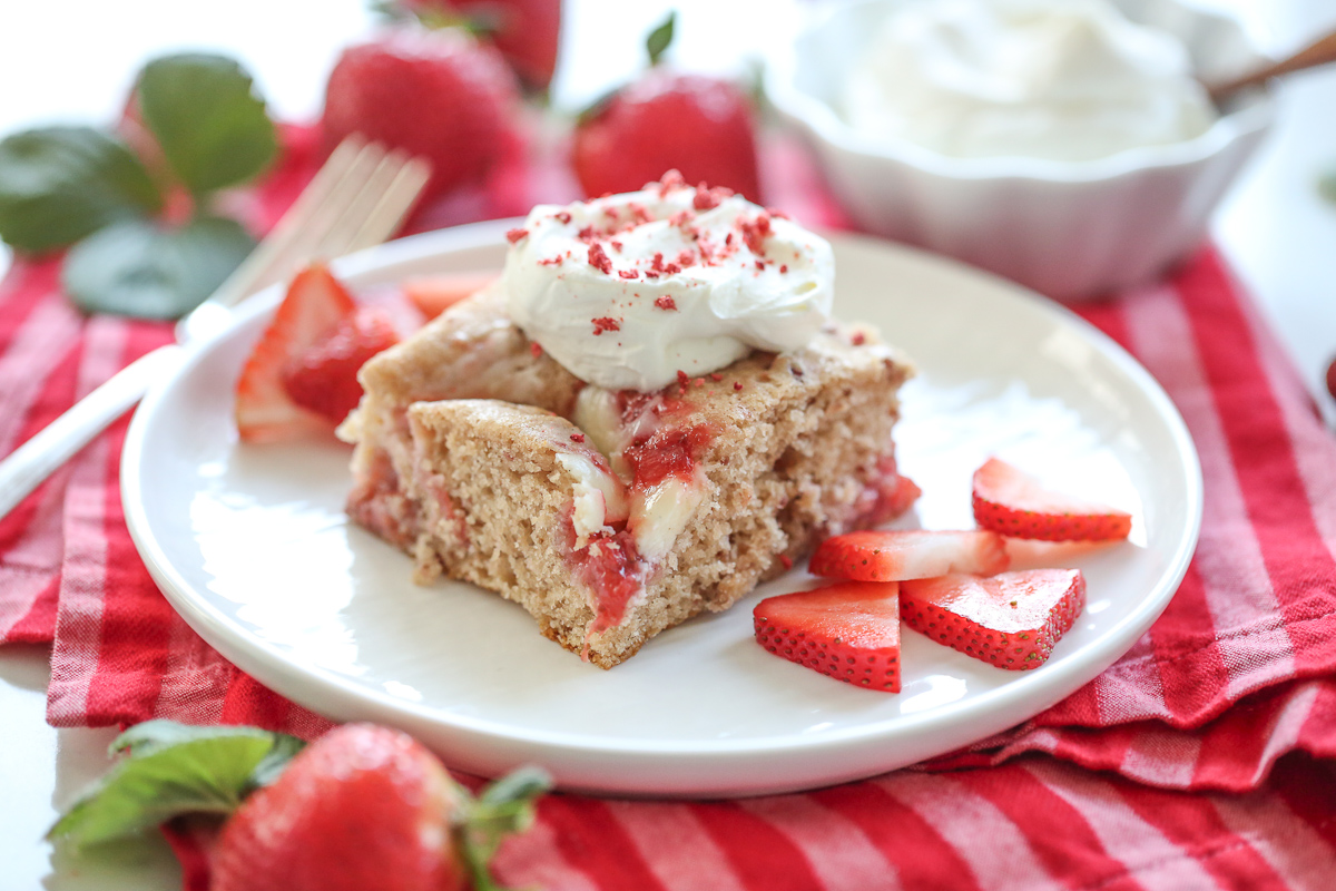Strawberry Cheesecake Swirl Cake on a white plate with berries and cream