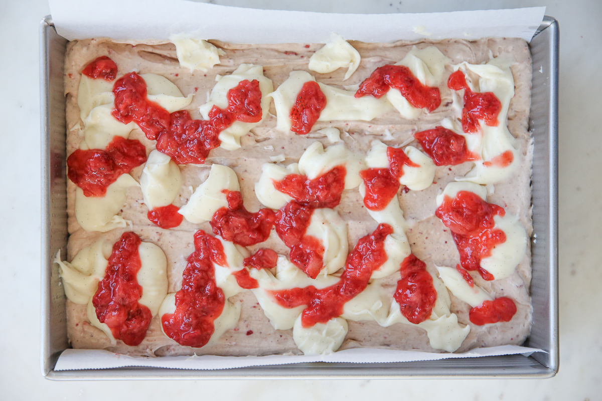 cake batter in a cake pan with cheesecake batter and berry compote swirled in